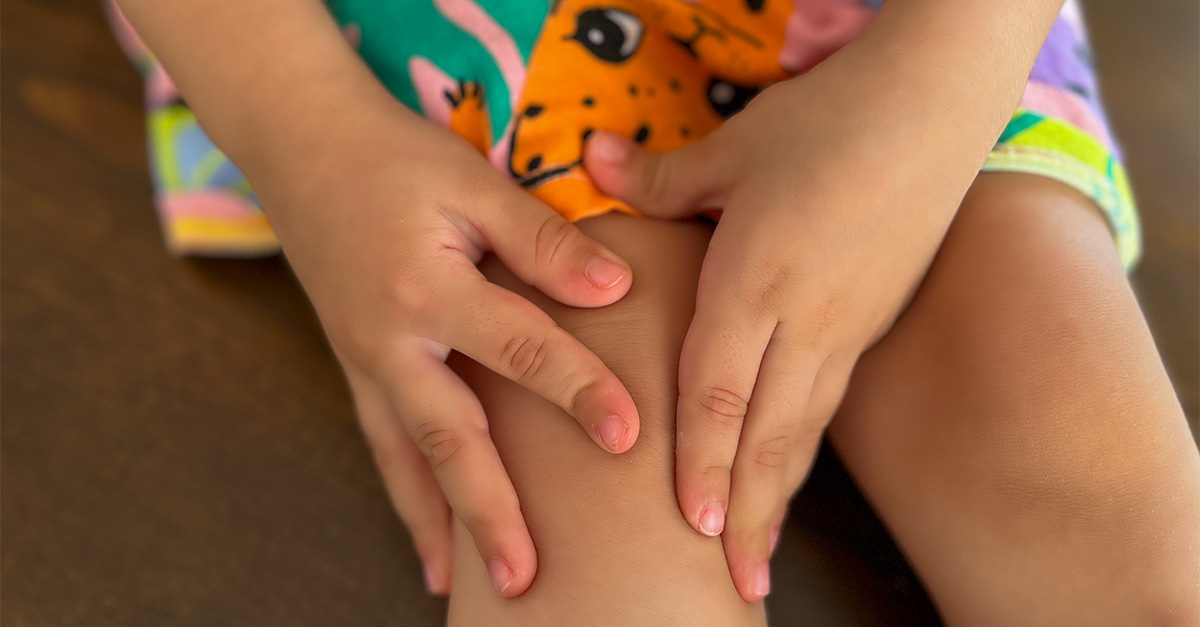 A child suffering from juvenile arthritis, holding her knee in pain.